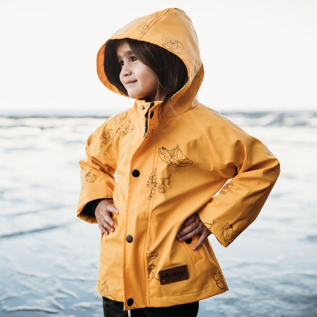 Waterproof Kids raincoat - Girl wears mustard yellow Wild Island Apparel waterproof rain jacket  with hood, with Australian designed native seedpod print in ethically made, more sustainable fabrics.